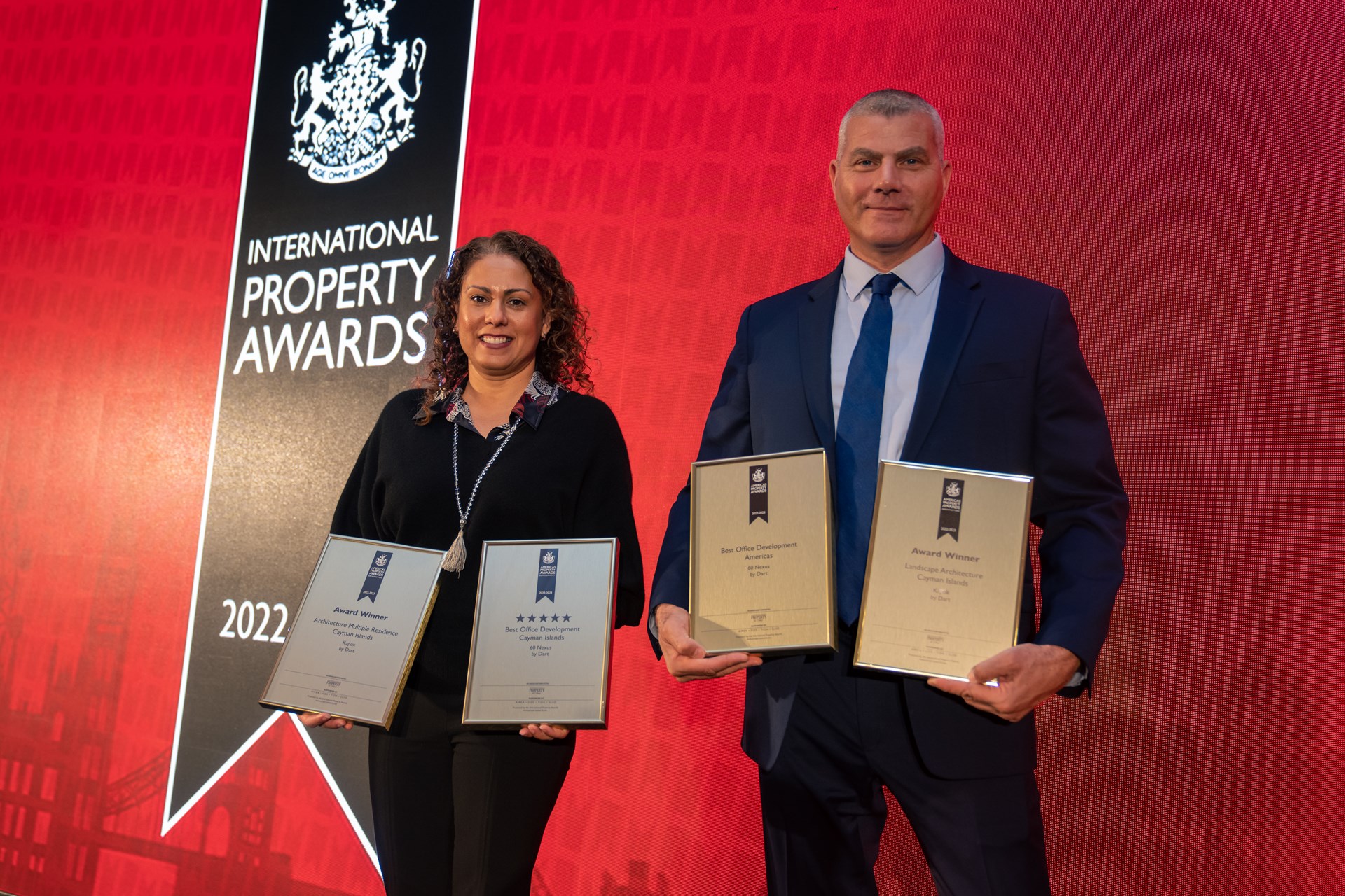 Man and woman stand next to each other holding awards